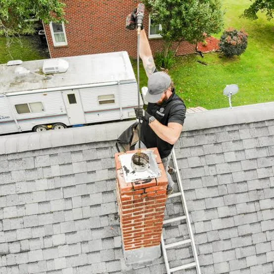 Chimney sweep cleaning a brick chimney from a residential rooftop.
