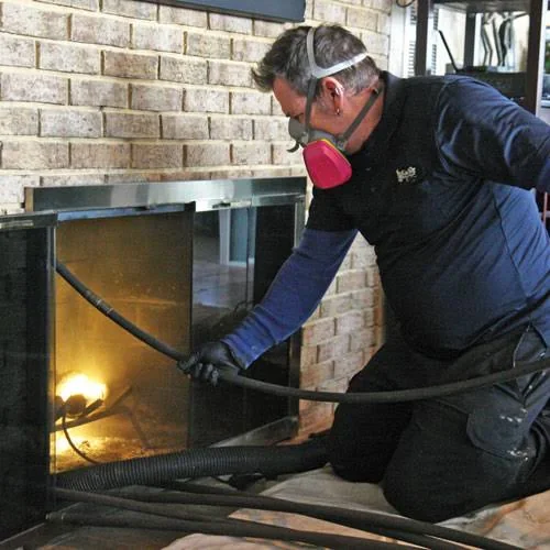 Person in protective gear cleaning the inside of an open fireplace with a hose and tool.