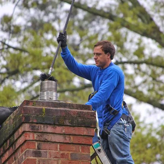 Worker in a safety harness cleaning a brick chimney with a long brush.