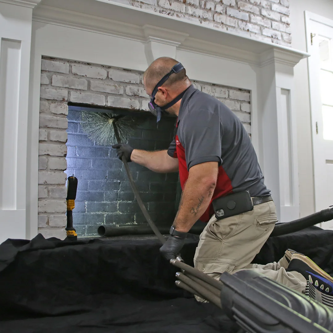Technician cleaning the inside of a brick fireplace with chimney-sweeping equipment.